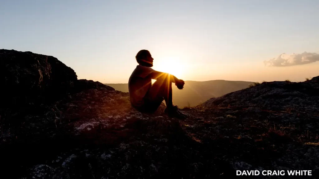 Person sitting alone at sunset, reflecting on life direction and personal clarity